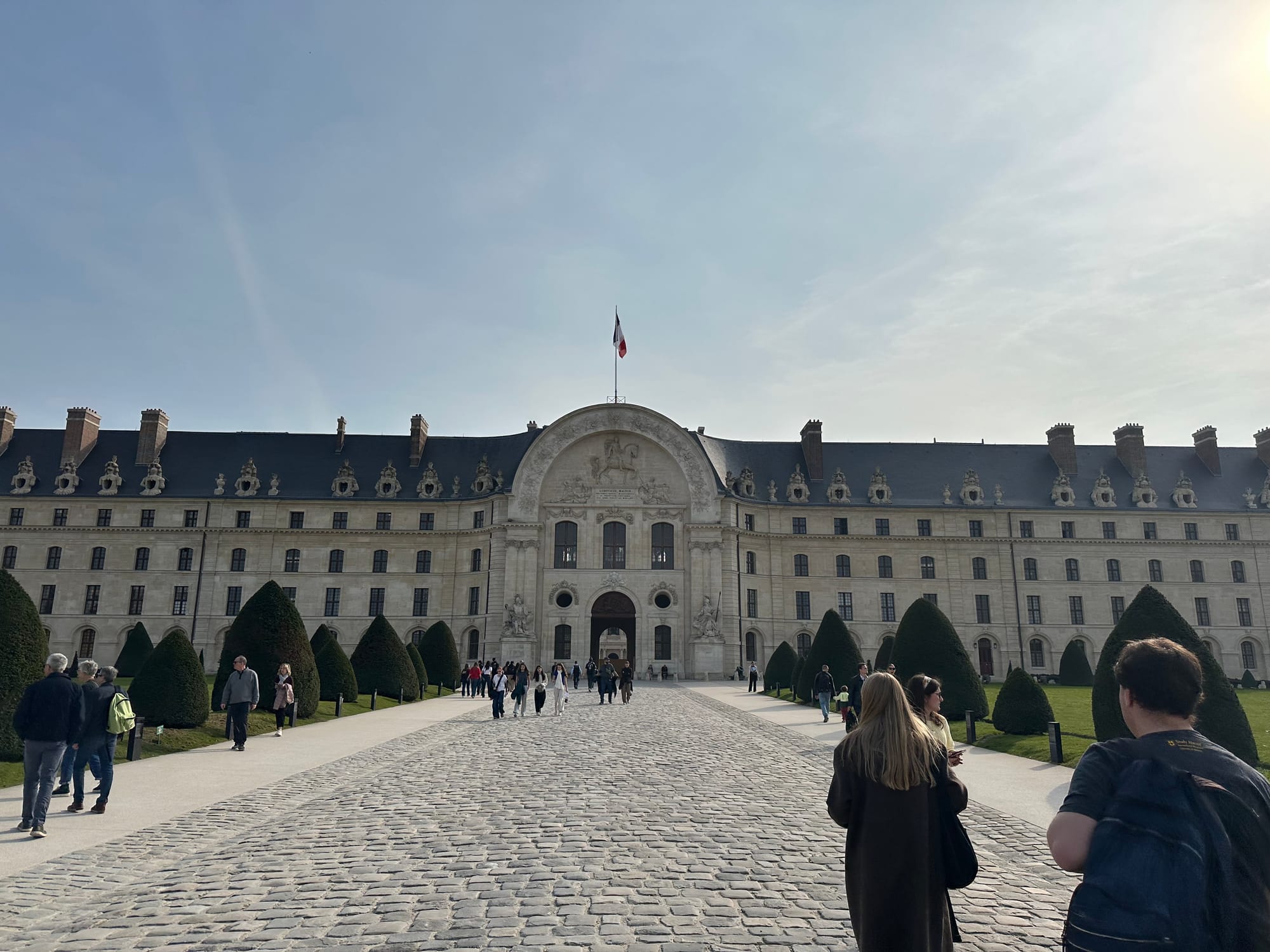 A long paved walkway to the front door of a long, 5 story building, the entrance to to Les Invalides